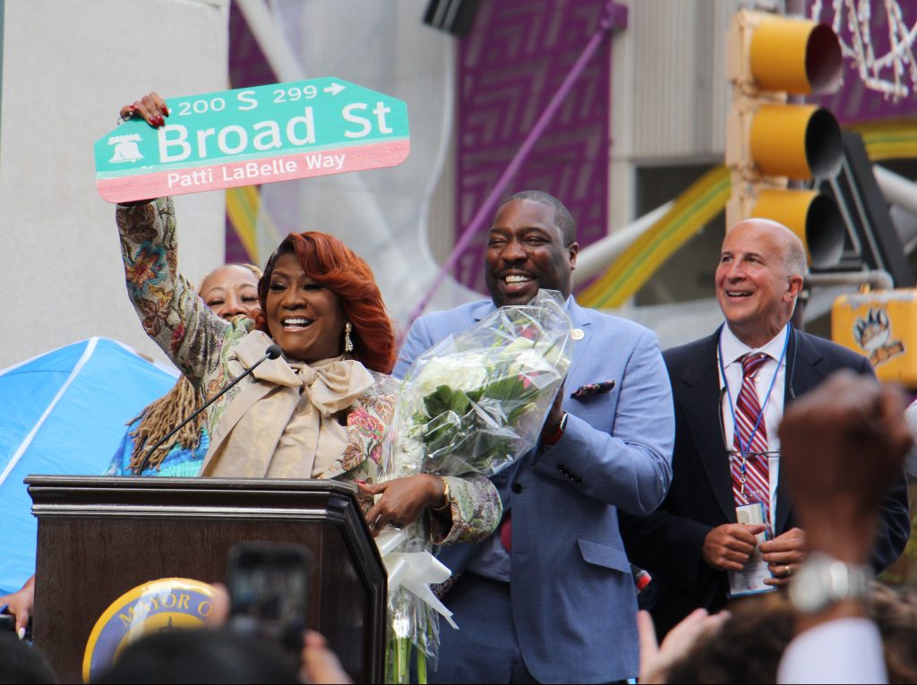 Image uploaded from iOS (9) Patti LaBelle holds up a sign named by a portion of Broad Street after her. (Emma Lee/WHYY)