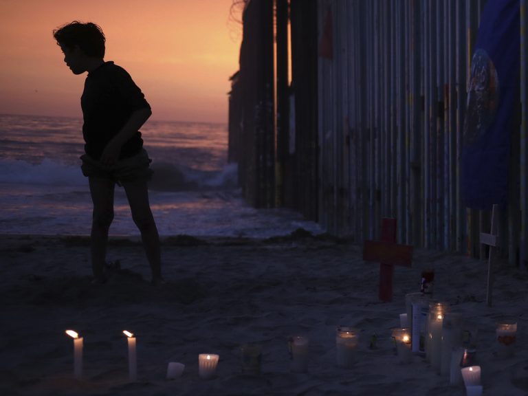 A youth stands Sunday by the border fence that separates Mexico from the U.S., where candles and crosses stand in memory of the father and daughter who died during their journey toward the U.S. (Emilio Espejel/AP)
