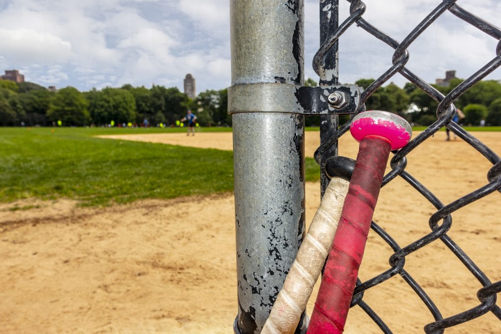 Two Bats At A Baseball Diamond Leaning On Bating Fence (Mirror-Images/Bigstock)