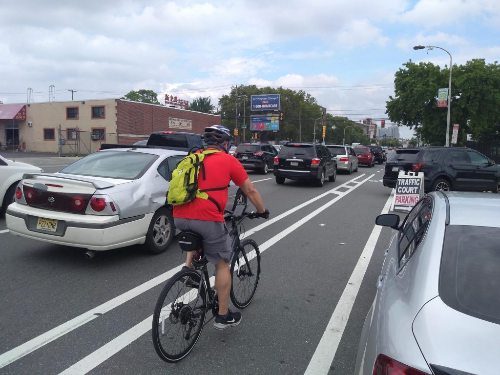 man-riding-his-bike-on-spring-garden-street-s-bike-line.original A bicyclist is shown from behind biking in a bike lane as cars go by them.