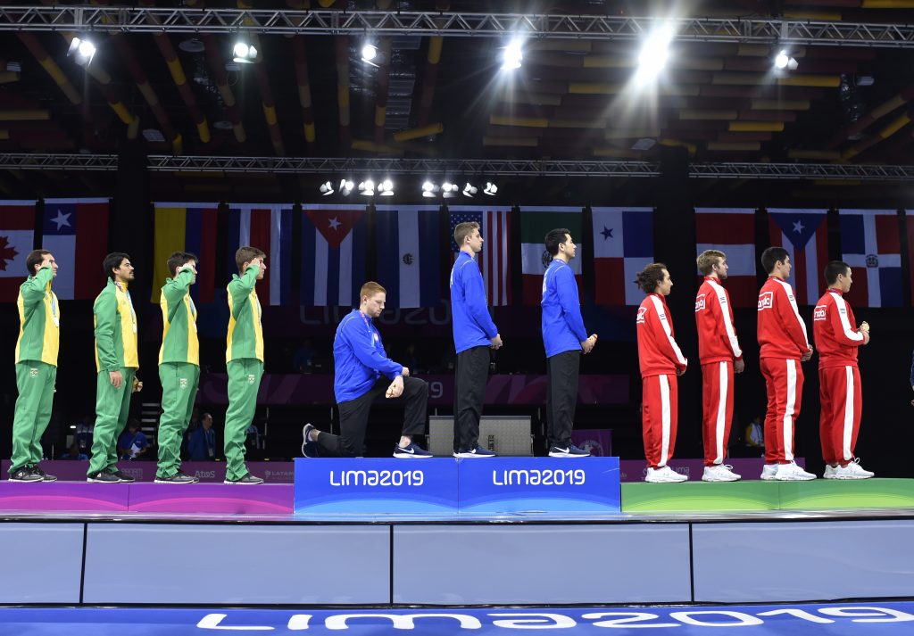 Peru Pan Am Games In this Friday, Aug. 9, 2019 photo, released by Lima 2019 News Services, Race Imboden of the United States takes a knee, as teammates Mick Itkin and Gerek Meinhardt stand on the podium after winning the gold medal in team's foil, at the Pan American Games in Lima, Peru. 'Racism, gun control, mistreatment of immigrants, and a president who spreads hate are at the top of a long list' of America's problems, Imboden said in a tweet sent after his medals ceremony. 'I chose to sacrifice my moment today at the top of the podium to call attention to issues that I believe need to be addressed.' (Jose Sotomayor/Lima 2019 News Services via AP)
