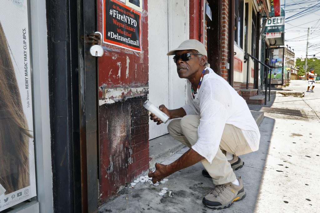 Doug Brinson collects candles to prevent a fire at the make-shift memorial, Tuesday, Aug. 20, 2019, where Eric Garner died in a police chokehold five years ago, in the Staten Island borough of New York. (Richard Drew/AP Photo)