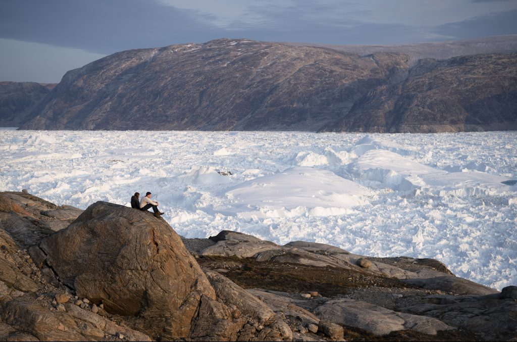 CORRECTION Trump Greenland In this Aug. 16, 2019, photo, New York University student researchers sit on a rock overlooking the Helheim glacier in Greenland. U.S. President Trump announced his decision to postpone an early September visit to Denmark by tweet Tuesday Aug. 20, 2019, after Danish Prime Minister Mette Frederiksen dismissed the notion of selling Greenland to the U.S. as