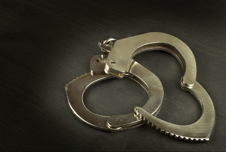 Metal police handcuffs on a dark wooden board.