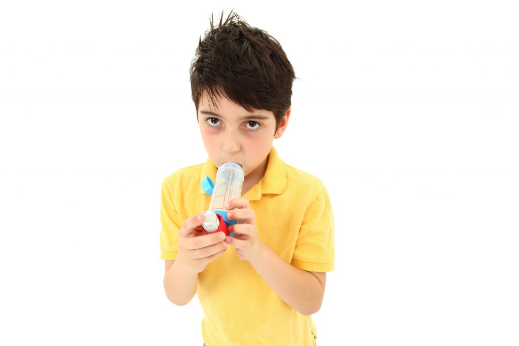 Boy Child Using Asthma Inhaler With Spacer Chamber Sick young boy child using asthma inhaler with spacer chamber over white. Has periorbital hyperpigmentation.