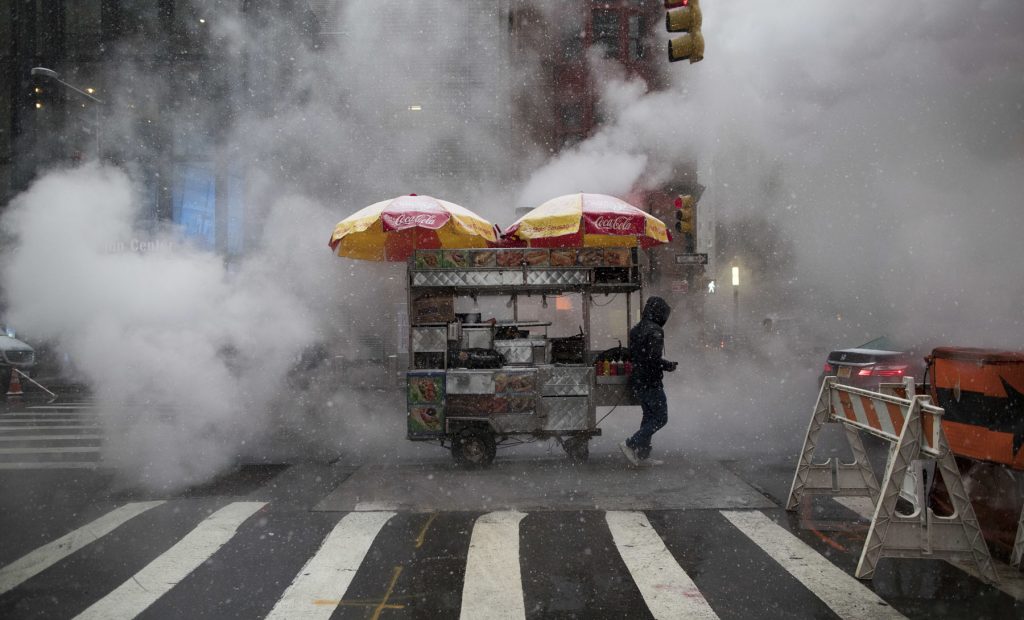 Winter Weather New York Snow falls on a street food vendor as he makes his way down Broadway with his cart past steam rising in New York, NY. (AP Photo/Mary Altaffer)