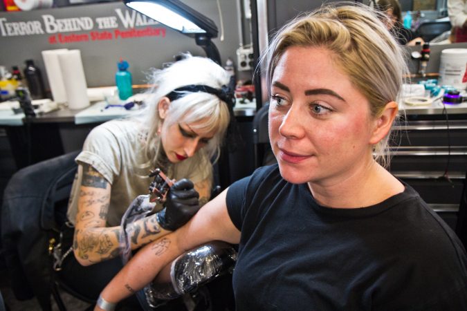 Kayleigh Geiger receives an origami-style bat tattoo from True Hand tattoo artist Arielle Coupe. She calls he assortment of little tattoos refrigerator magnets. (Kimberly Paynter/WHYY)