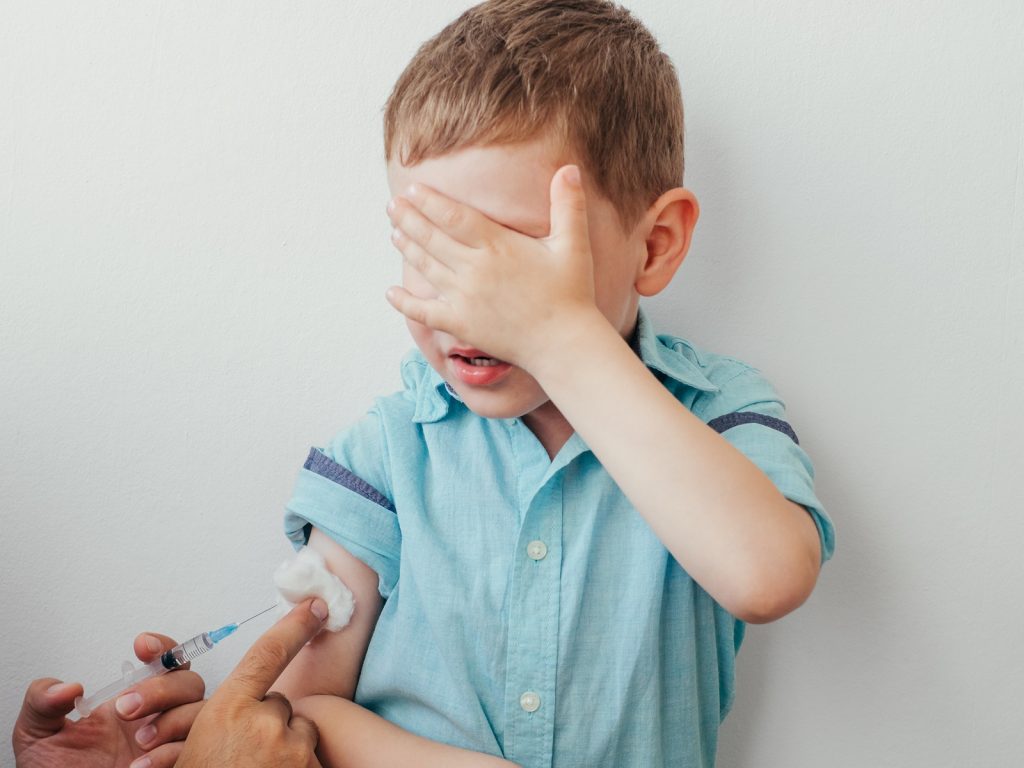 Little Boy Is Afraid To Vaccinate. Little Caucasian Baby Boy In Blue Shirt Covered His Eyes With Han (Fascinadora/Bigstock)