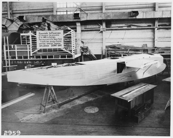 Hull of an experimental F6L flying boat under construction at the Naval Aircraft Factory, Philadelphia Naval Shipyard, with influenza precaution sign in background, October 19, 1918. (U.S. Naval History and Heritage Command Photograph, Catalog # NH 41731, Archives Branch, Naval History and Heritage Command, Washington, D.C.)
