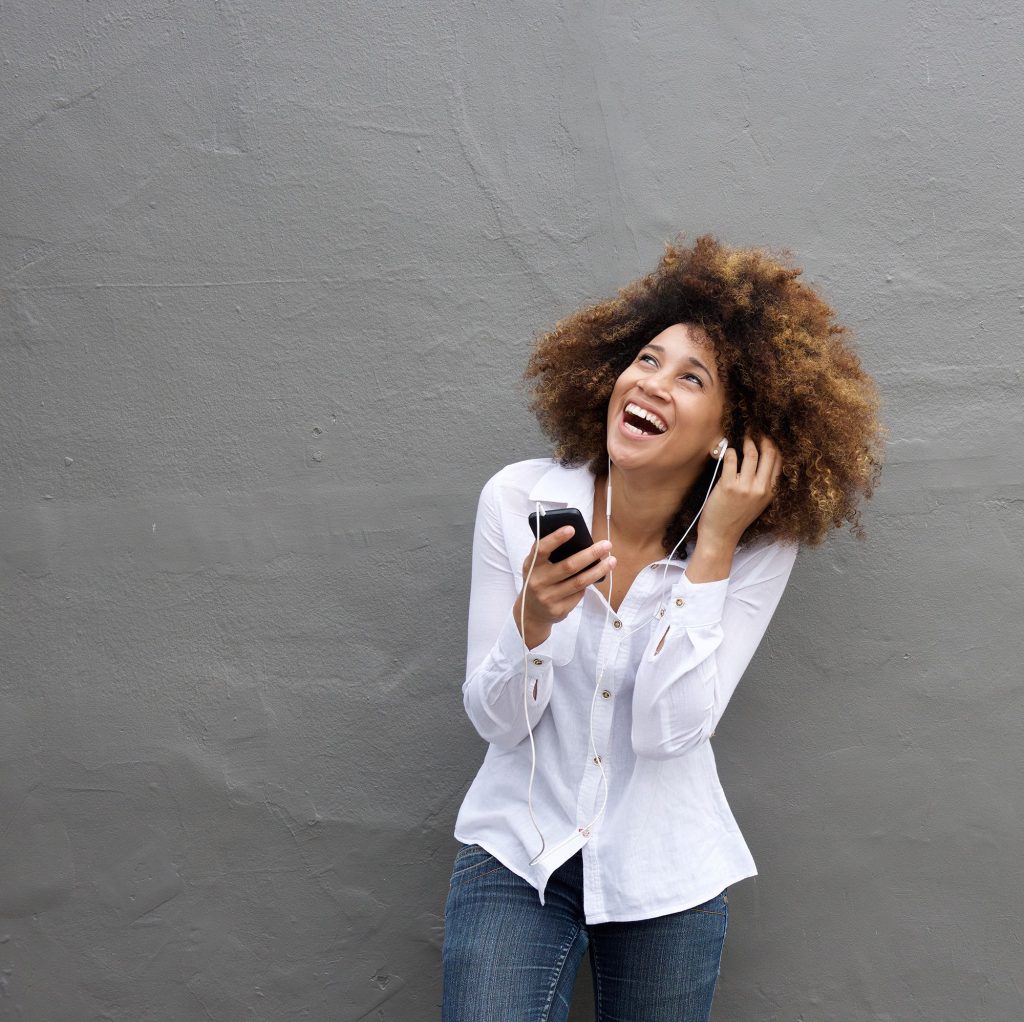Laughing young woman listening to music on cell phone (m-imagephotography/iStock)