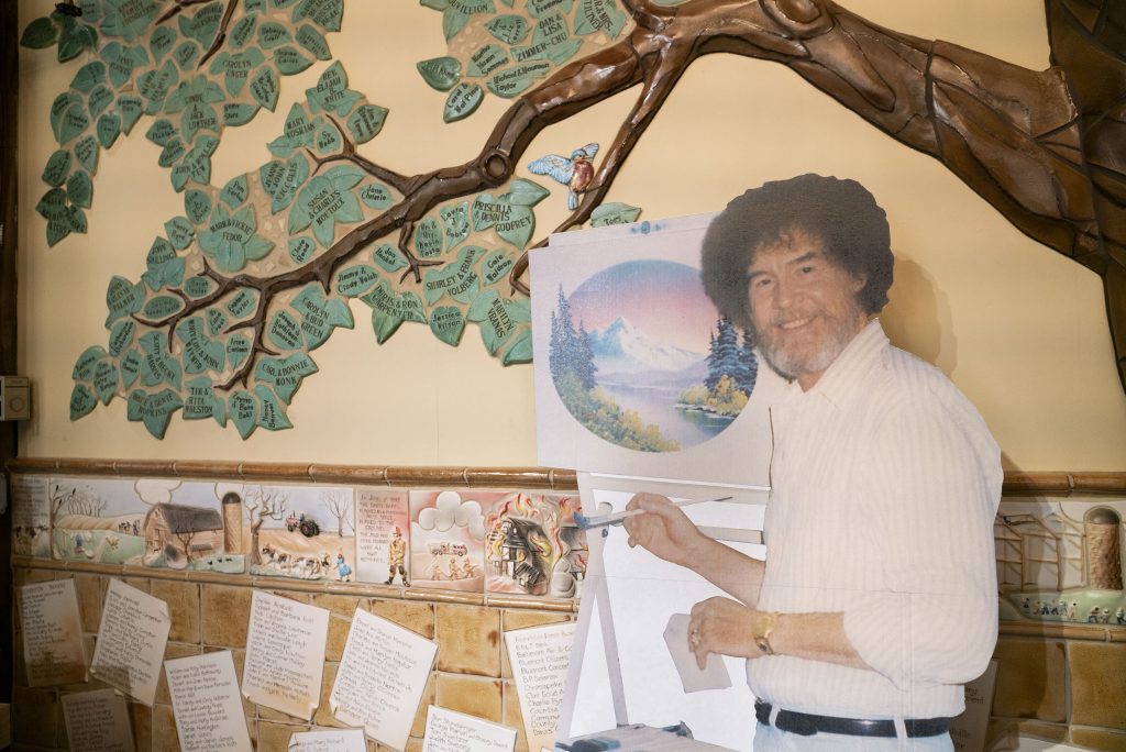 A life size cut out of Bob Ross stands up against the wall where the historical tree of the Franklin Park Arts Center is painted. Bob Ross Inc. is located in Herndon, Va., which is only 27 miles from the exhibit. According to managing director, Elizabeth Bracey, the exhibit was intentionally kept close to headquarters. A life size cut out of Bob Ross stands up against the wall where the historical tree of the Franklin Park Arts Center is painted. Bob Ross Inc. is located in Herndon, Va., which is only 27 miles from the exhibit. According to managing director, Elizabeth Bracey, the exhibit was intentionally kept close to headquarters. (Mhari Shaw/NPR)