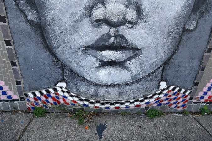 A small orange syringe cap and a plastic bag lay next to a mural near Lewis Elkin Elementary School. (Bastiaan Slabbers for WHYY)