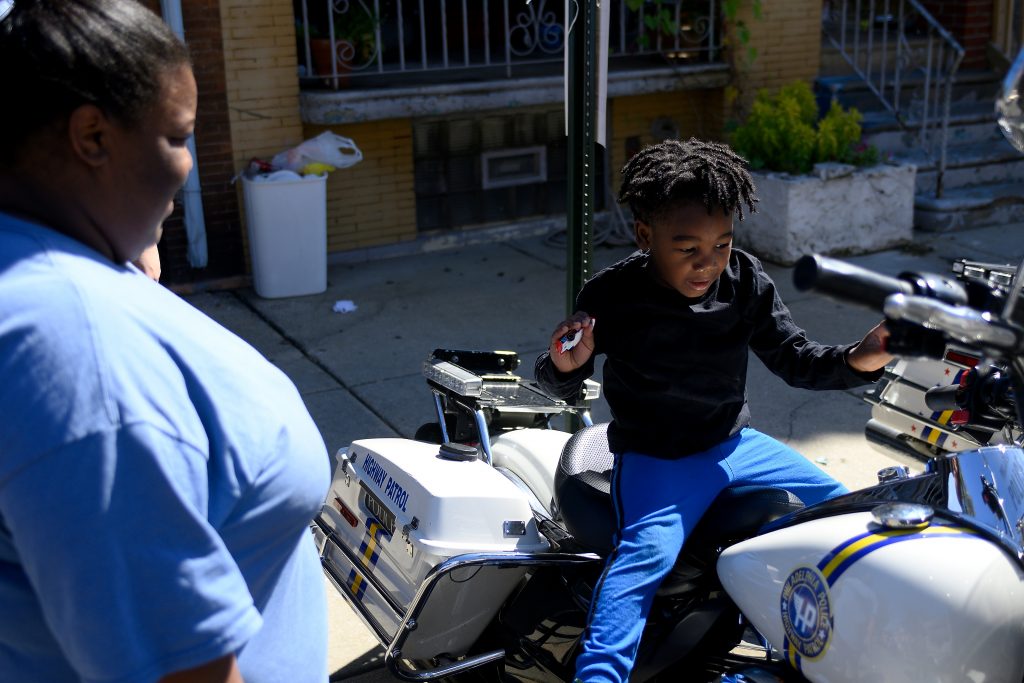 Love Peace and Soul Fest Octavia Abney watches her son Dylan, 4, sit on a Philadelphia Police Department motorbike during the Love Peace and Soul Fest block party on Sunday October 5, 2019 at the site of the August Police shooting and stand off in the Nicetown-Tioga section of Philadelphia. (Bastiaan Slabbers for WHYY)