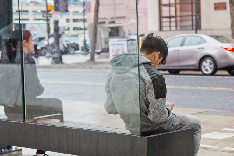 A commuter listens to music while they wait for a SEPTA bus. (Kimberly Paynter/WHYY)