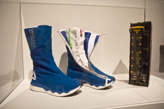 Space boots designed by Reebok and a cubesat, a small device designed to collect data in space, at the Designs for Different Futures exhibit at the Philadelphia Art Museum. (Kimberly Paynter/WHYY)