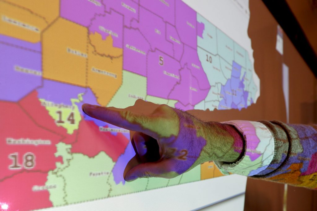 AP_18320699374231-1920×1280 William Marx points out one of the districts that crossed four counties as an image of the old congressional districts of Pennsylvania are projected on a wall in the classroom where he teaches civics in Pittsburgh on Friday, Nov. 16, 2018. Marx was a plaintiff in the Pennsylvania lawsuit that successfully challenged the Republican-drawn congressional maps. Marx said he believes the new district boundaries resulted in