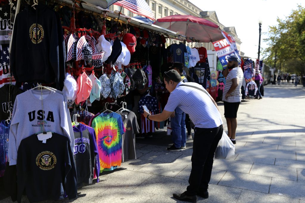 China Trade War Reassuring Tourists In this Oct. 15, 2019, photo a Chinese tourist takes pictures of Washington DC t-shirts at a tourism kiosk in Washington. (Bani Sapra/AP Photo)