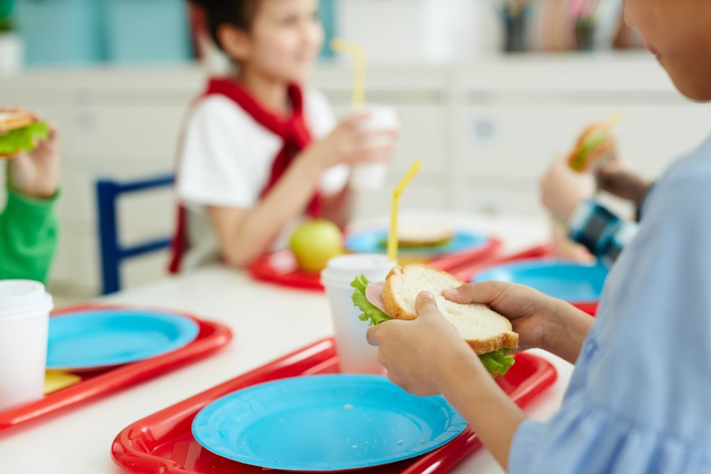 Unrecognizable children sitting at table and eating tasty sandwiches while having lunch in elementar (pressmaster/BigStock)