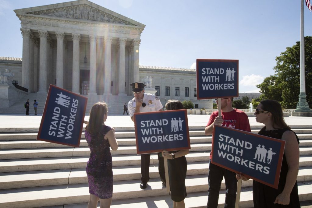 union-dues-government-workers-1920×1280 People gather at the Supreme Court awaiting a decision in an Illinois union dues case, Janus vs. AFSCME, in Washington, Monday, June 25, 2018. The outcome of that case and several others were not announced Monday as the court's term comes to a close. (J. Scott Applewhite/AP Photo)