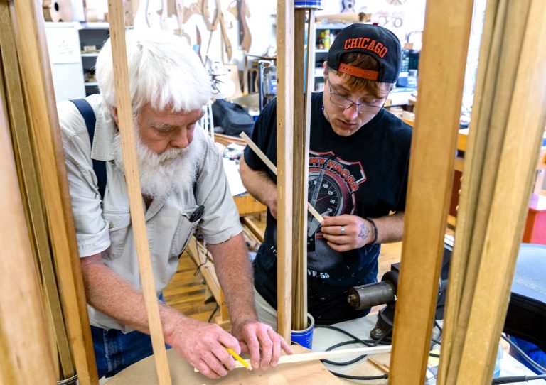 Paul Williams (left) helps Scott Beatty build his 'backpack' guitar. It has a smaller body, meant to easily fit in a pack. Beatty is in the Culture of Recovery program which teaches instrument making to people recovering from addiction. (Caitlin Tan/West Virginia Public Broadcasting)
