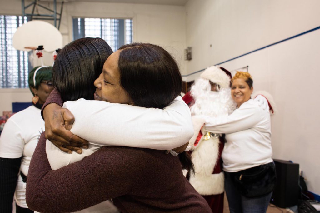 2019 12 08-b haydu-philadelphia pennsylvania south philadelphia dixon house-moms bonded by grief christmas holiday party-17 Danielle Shaw (center) embraces a fellow member of Moms Bonded By Grief at a holiday party in South Philadelphia on Dec. 8, 2019. (Becca Haydu for WHYY)