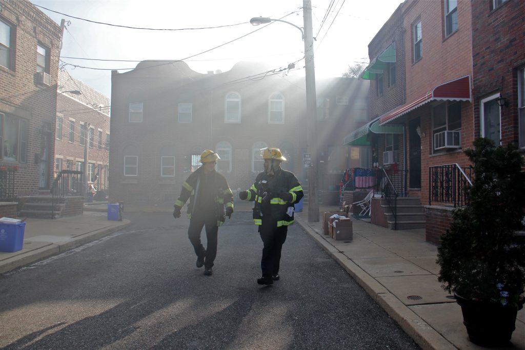 2019 12 19-e lee-philadelphia south 8th street-rowhouse fire Firefighters walk through a smoke haze on South Beulah Street, checking on residents near the scene of a 3-alarm fire in the 1400 block of South 8th Street. (Emma Lee/WHYY)