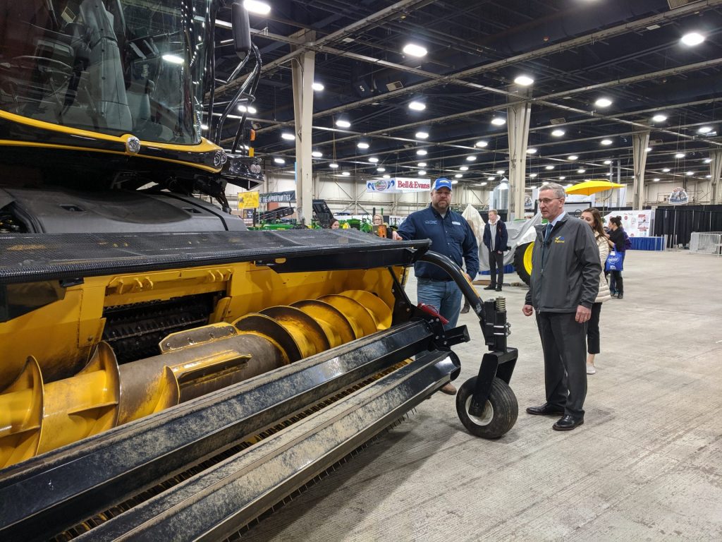 IMG_20191230_101721-1920×1440 Agriculture Secretary Russell Redding (right) looks at a piece of harvesting equipment with Jason Forrester of Forrester Farm Equipment in Chambersburg, Pa. Redding was giving a tour at the Pennsylvania Farm Show Complex on Monday, December 30, 2019. (Rachel McDevitt/WITF)