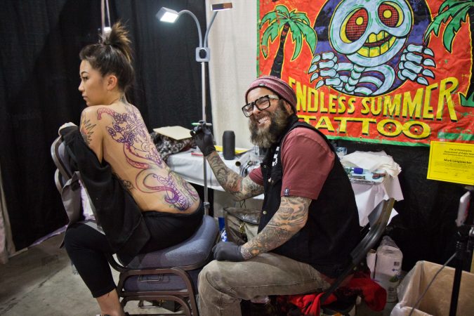Mark Longenecker prepares to tattoo Tibetan skulls and an octopus on the back of Lindy Klensoki at the 2020 Philadelphia Tattoo Convention. (Kimberly Paynter/WHYY)