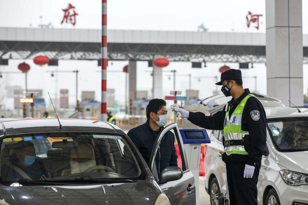 In this Jan. 23, 2020, file photo, a policeman uses a digital thermometer to take a driver's temperature at a checkpoint at a highway toll gate in Wuhan in central China's Hubei Province. Cutting off access to entire cities with millions of residents to stop a new virus outbreak is a step few countries other than China would consider, but it is made possible by the ruling Communist Party's extensive social controls and experience fighting the 2002-03 outbreak of SARS. (Chinatopix via AP)