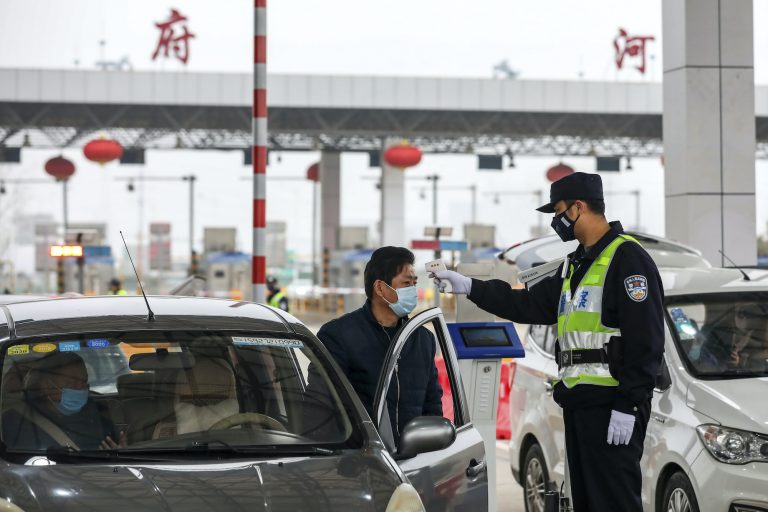 In this Jan. 23, 2020, file photo, a policeman uses a digital thermometer to take a driver's temperature at a checkpoint at a highway toll gate in Wuhan in central China's Hubei Province. Cutting off access to entire cities with millions of residents to stop a new virus outbreak is a step few countries other than China would consider, but it is made possible by the ruling Communist Party's extensive social controls and experience fighting the 2002-03 outbreak of SARS. (Chinatopix via AP)