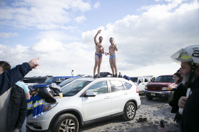 Pete Stanfer, left, and William Dean dance on top of their car during the 2020 polar bear plunge in Margate, NJ on Wednesday, January 1, 2020. (Miguel Martinez for WHYY)