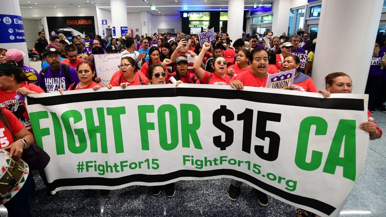 Airport employees, Uber and Lyft drivers, and other workers protest for a $15 minimum wage at Los Angeles International Airport in October. Increases in minimum wages contributed to bigger pay gains for lower-income workers. (Frederic J. Brown/AFP via Getty Images)