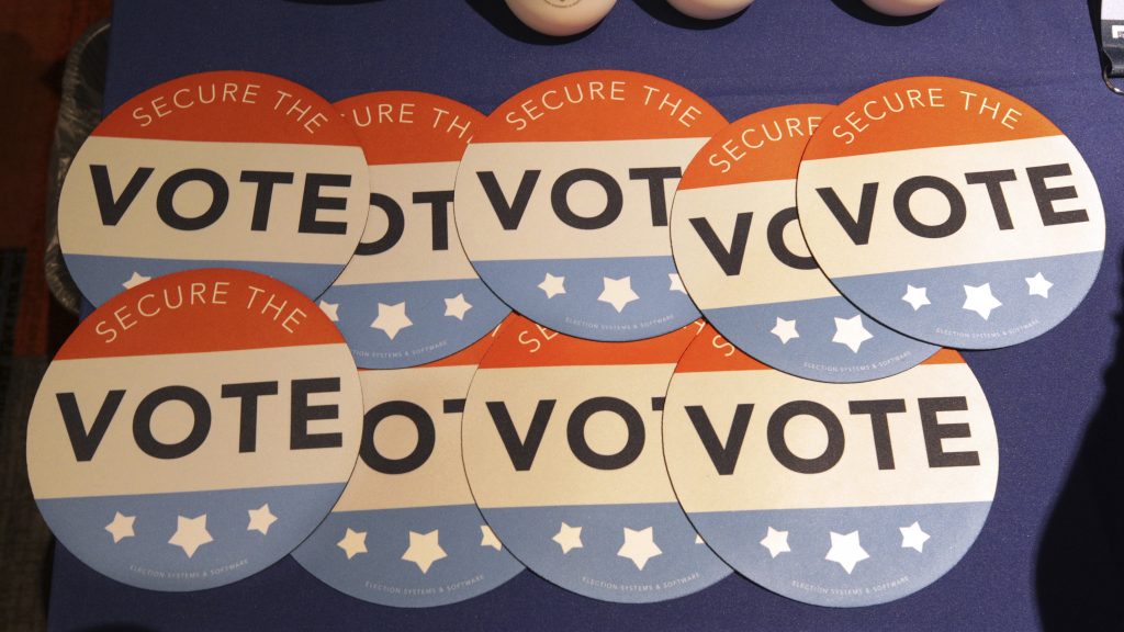 Computer mouse pads with “Secure the Vote” logos on them sit on a vendor’s table at an election officials conference in 2018. Computer mouse pads with