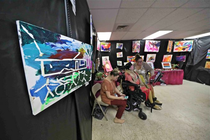 Haley Shiber (center) is seen surrounded by her paintings during an art therapy exhibit on Feb. 10, 2020, at The Art Studio in Wilmington, Del. (Saquan Stimpson for WHYY)