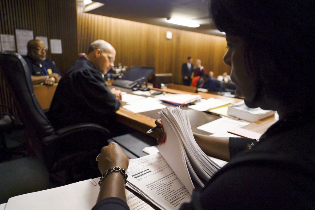 AP_17244527118234 MAIN In this Aug. 30, 2017, photo, Stephanie Pope-Earley, right, sorts through defendant files scored with risk-assessment software for Jimmy Jackson Jr., a municipal court judge, on the first day of the software's use in Cleveland. In a growing number of local and state courts, including Cleveland, judges are now guided by computer algorithms before ruling whether criminal defendants can return to everyday life, or remain locked up awaiting trial. (Dake Kang/AP Photo)