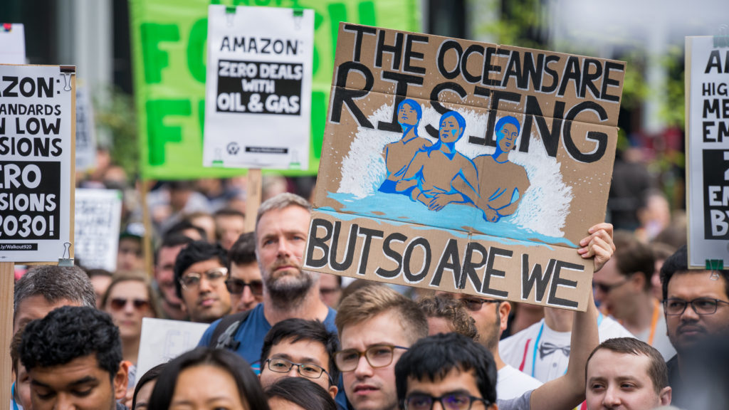 A protester holds a sign reading “The Oceans Are Rising But So Are We” at an Amazon employee walkout in Seattle, as part of the Global Climate Strike on Sept. 20, 2019. At some companies, employees are putting increasing pressure on their bosses to act on climate change. A protester holds a sign reading