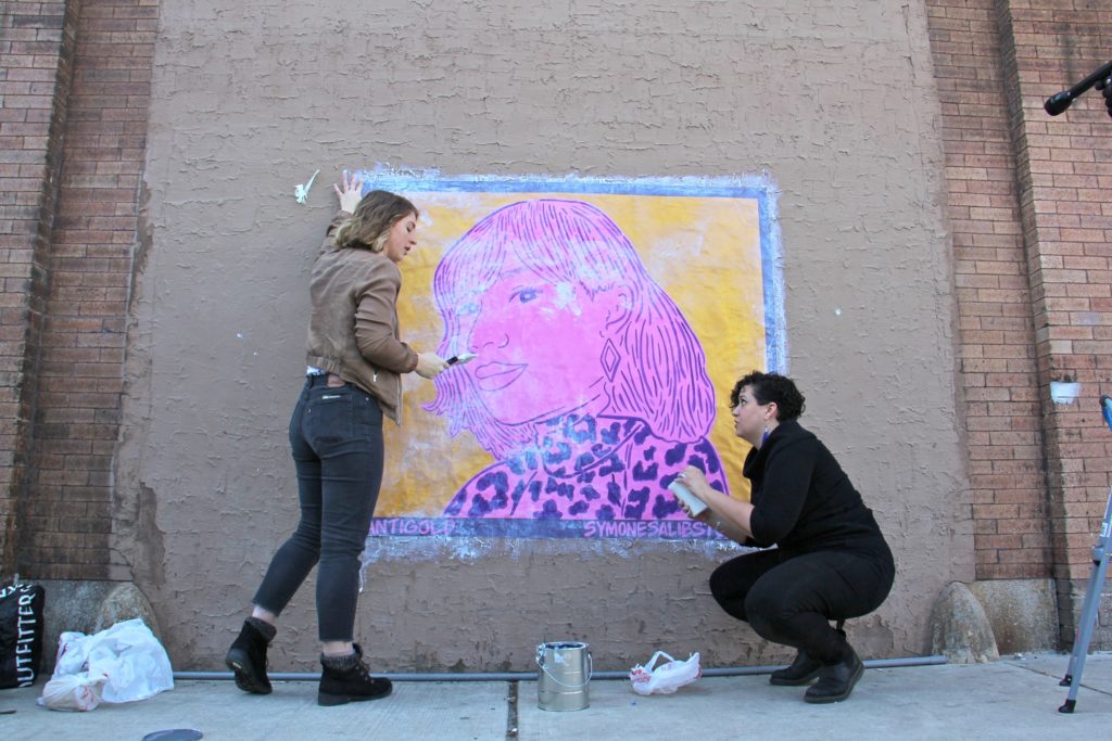 2020 03 05-e lee-nicole nikolich symone salib-philadelphia-sisterlylove project murals santigold Nicole Nikolich (left) and Symone Salib install Salib's wheat paste portrait of Santigold on a wall of The Filmore. The work is one of 20 in the #SisterlyLove Project, celebrating 20 Philadelphia women during Women's History Month. (Emma Lee/WHYY)