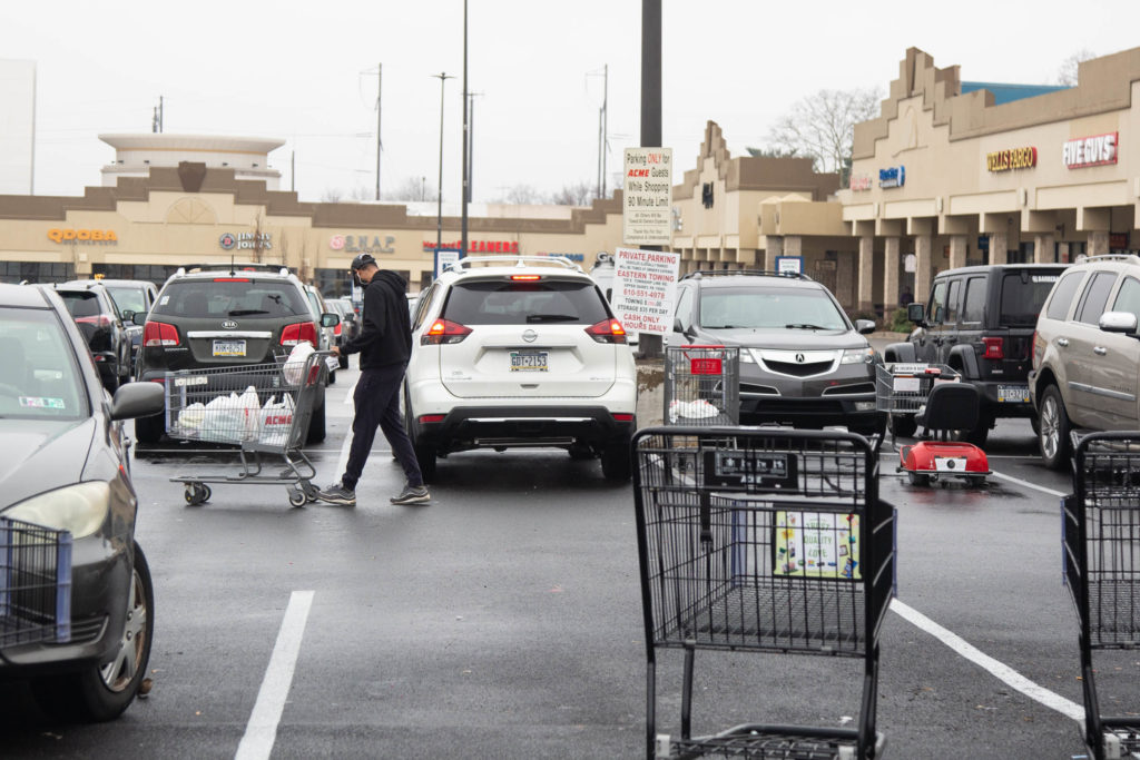 2020 03 19- ecohen- wide shot of unnamed shoppers – bala cynwyd – acme shoppers – covid19-1 Carts litter the parking lot around 9 a.m. as a shopper heads back to their car with groceries after shopping at the ACME in Bala Cynwyd on March 19th 2020 during the uncertain times that surround the Covid 19 pandemic. (Emily Cohen for WHYY)