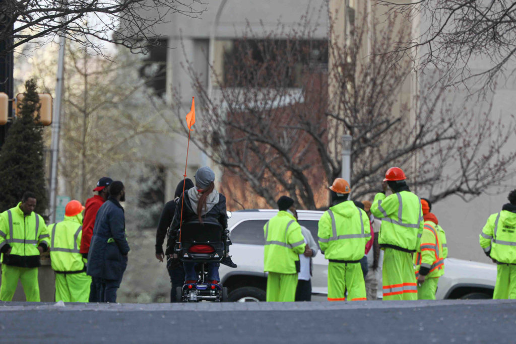 News 2020 – Mar 26 – Wilmington Delaware sees a reduction in activity due to the stay at home order. A pedestrian uses her scooter on Market Street in Wilmington, Del., as she approaches a group of construction workers on Thursday, March 26, 2020. (Saquan Stimpson for WHYY)
