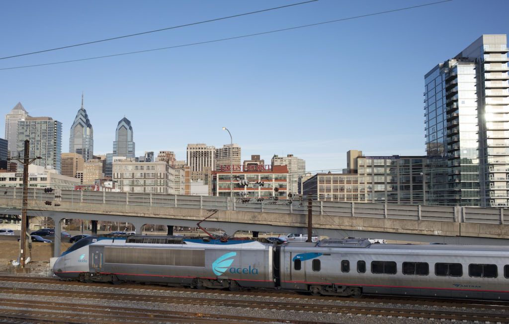 A train speeds by, as Philadelphia skyline is visible in the background.