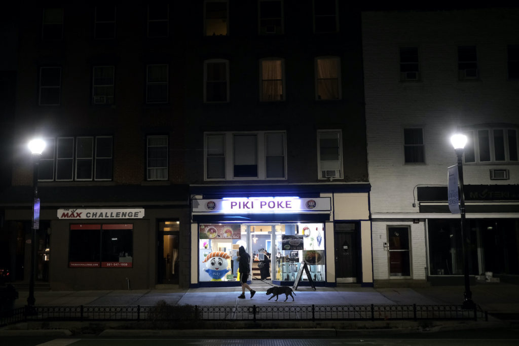 A man walks his dog on a mostly empty street before the start of a 10 p.m. curfew in Hoboken, N.J., Tuesday, March 17, 2020. (Seth Wenig/AP Photo)