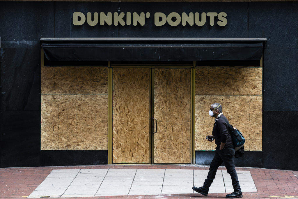 A person wearing protective masks due to coronavirus fears walks past a boarded up business in Philadelphia, Tuesday, March 24, 2020. (AP Photo/Matt Rourke)