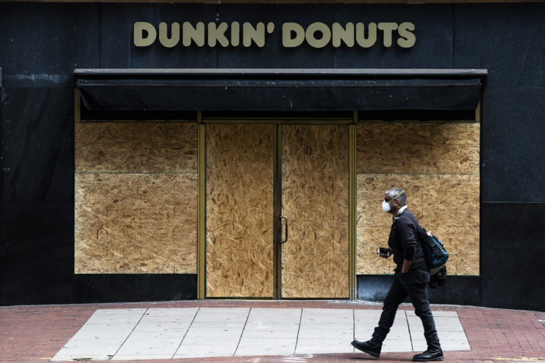 A person wearing protective masks due to coronavirus fears walks past a boarded up business in Philadelphia, Tuesday, March 24, 2020. (AP Photo/Matt Rourke)