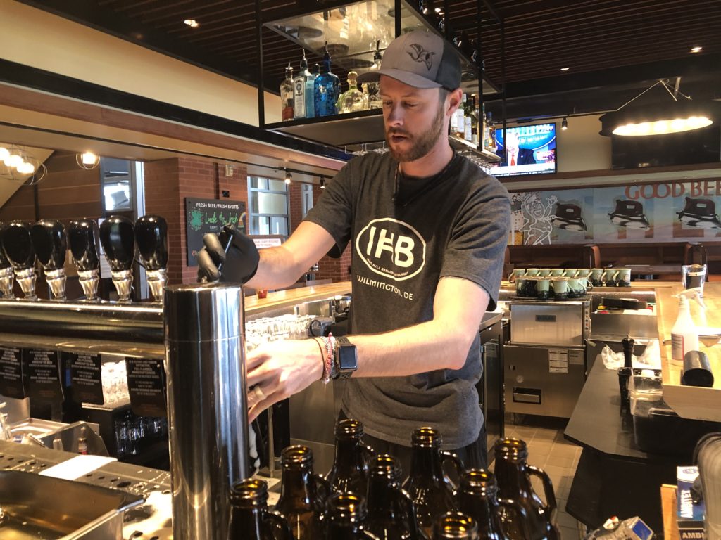 Dustin Mitchell fills up a growler for take-out orders at Iron Hill Brewery. (Cris Barrish/WHYY)