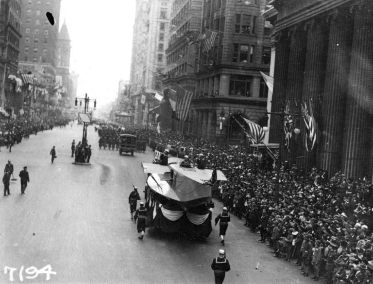 A Naval Aircraft Factory float, featuring the hull of a F5L patrol seaplane, heads south on Broad Street in Philadelphia, escorted by sailors with rifles. Note the crowd of onlookers. This parade, with its associated dense gatherings of people, contributed significantly to the massive outbreak of influenza which struck Philadelphia a few days later. (NH 41730 courtesy of the Naval History & Heritage Command)
