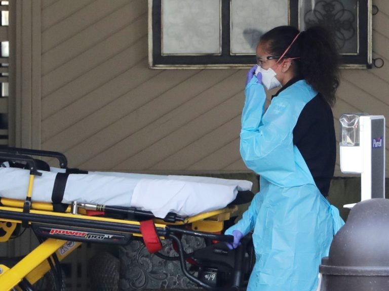 An ambulance worker adjusts her protective mask as she wheels a stretcher into a nursing facility in Kirkland, Wash., on Saturday where more than 50 people were found to be sick and are being tested for COVID-19 virus. (Elaine Thompson/AP Photo)