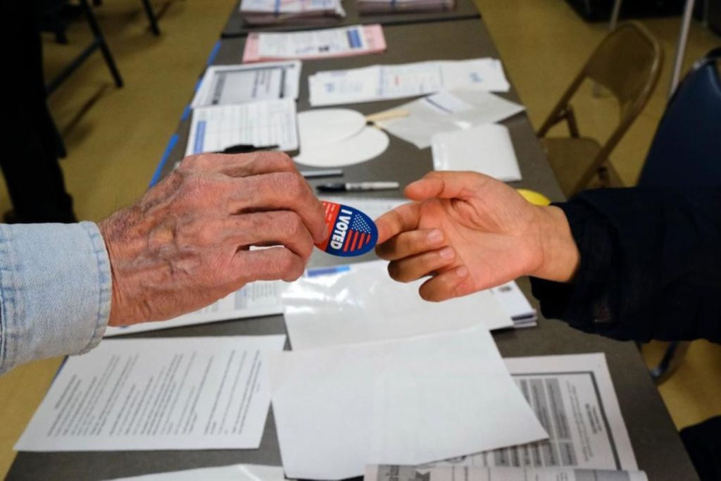voting-sticker-hands3-1920×1281 A voter receives his I-Voted sticker, at an early voting polling station at the Ranchito Avenue Elementary School in the Panorama City section of Los Angeles on Monday, March 2. (Richard Vogel/AP Photo)