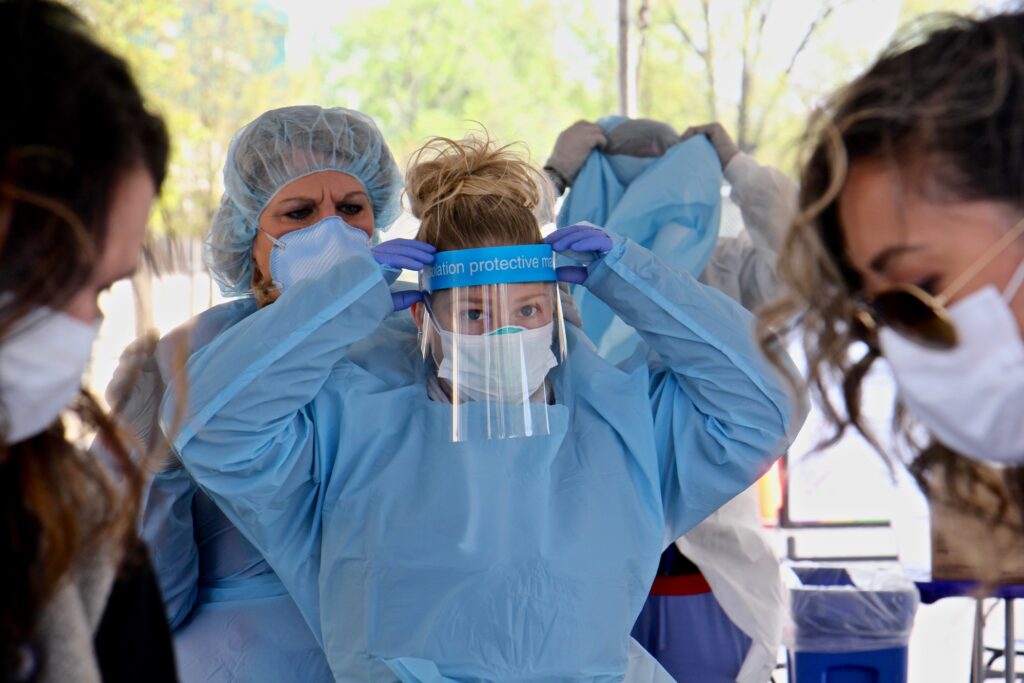 2020 04 29-e lee-camden nj-covid testing site Medical assistant Michelle Gravinese (left) helps her colleague Kayla Clauso put on protective gear before administering COVID-19 tests at a testing site in the Motor Vehicle Commission parking lot in Camden, New Jersey. (Emma Lee/WHYY)