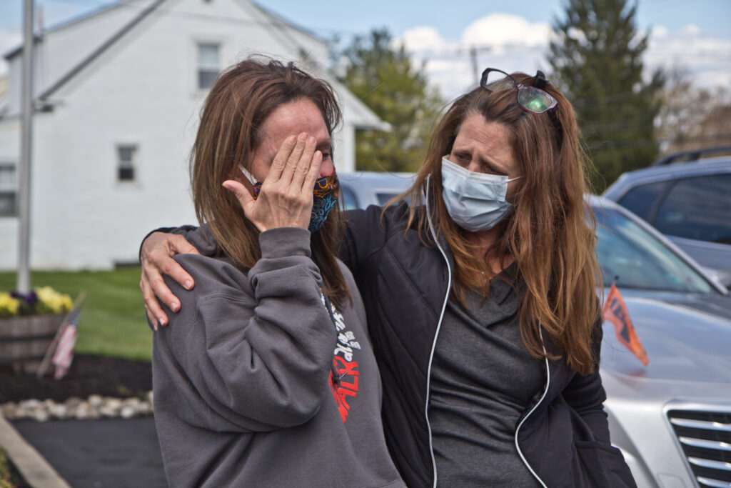 2020 4 21 k paynter covid death procession for marine-5 Tammy King (left) is comforted by her sister Michelle Rouco, both nurses, who were not allowed to see their father before he succumbed to COVID-19. (Kimberly Paynter/WHYY)