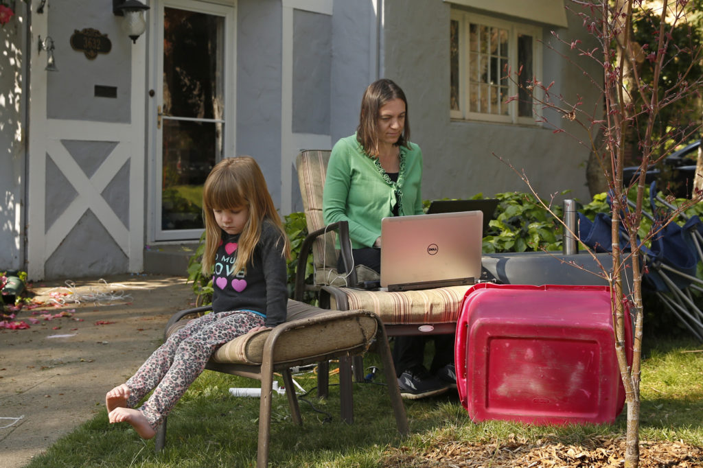 Virus Outbreak California Alison Steffensen is joined by her daughter, Elin, 3, as she works at the home office she set up in the front yard of her home in Sacramento, Calif., Friday, March 20, 2020. (AP Photo/Rich Pedroncelli)